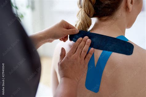 chinese woman massage therapist applying kinesio tape to the shoulders and neck of an attractive