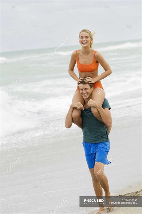 Hombre cargando mujer en hombros en la playa Traje de natación Ocio Stock Photo