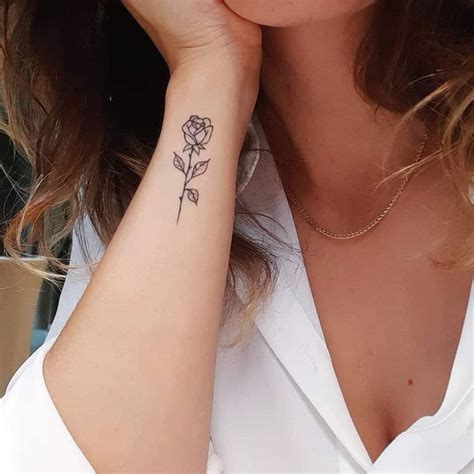 A Woman With A Rose Tattoo On Her Left Wrist And Right Hand Behind Her Ear
