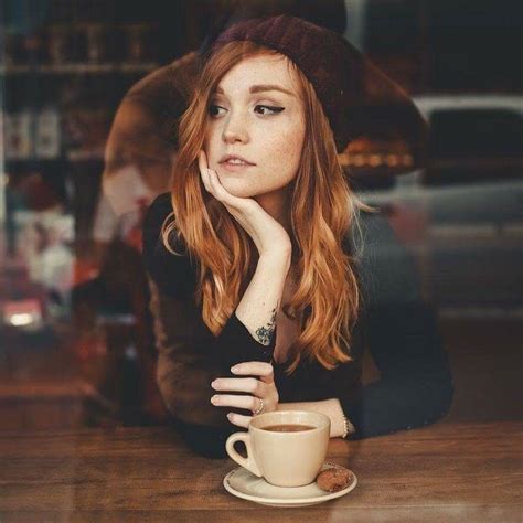 A Woman Sitting At A Table With A Cup Of Coffee In Front Of Her Face