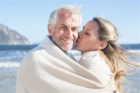 premium photo smiling couple wrapped up in blanket on the beach