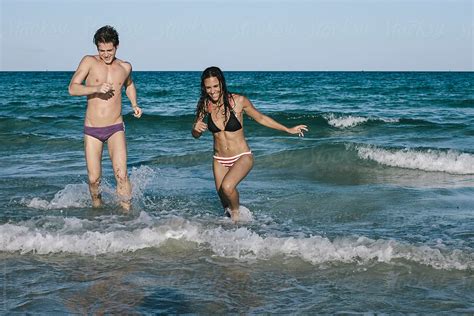 Playful Young Couple In Bikini And Trunks Having Fun At The Beach In