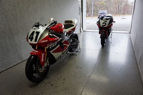 Two Red And White Motorcycles Parked In Front Of An Open Garage Door