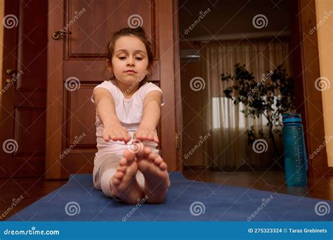 Adorable Child Girl Doing Stretching Exercises Sitting Barefoot On Gym