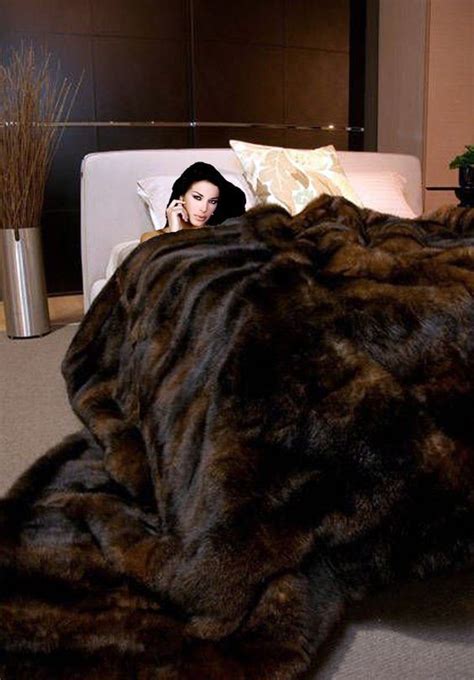 A Woman Laying On Top Of A Bed Covered In A Large Brown Fur Blanket Next To A White Couch