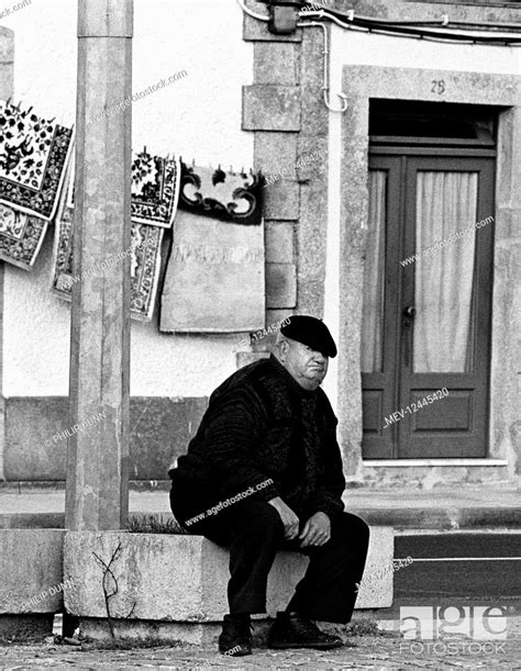 a fat old man with grumpy expression looks at the camera as he sits in the street in esposende