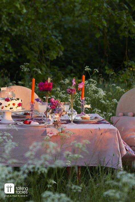 A Table Set For Two With Flowers And Candles On It In The Middle Of Some Tall Grass