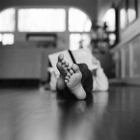 Young Girl Laying On Hardwood Floor Reading A Book With Only Her Feet