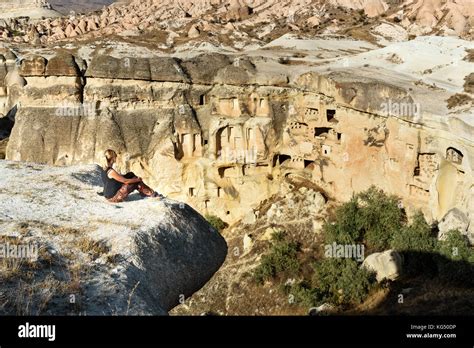 Woman Tourist Sitting On Cliff View Of Cave Houses In Rock At Cavusin