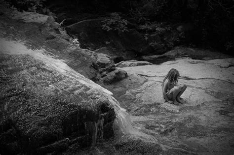 A Woman Sitting On Top Of A Large Rock Next To A Waterfall In Black And White