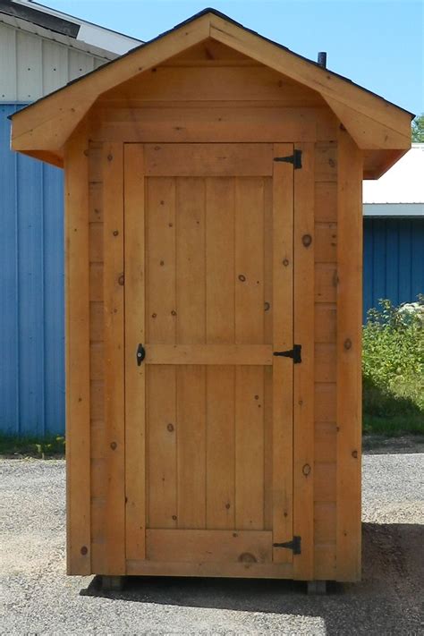 A Small Wooden Outhouse Sitting In The Middle Of A Gravel Lot Next To A