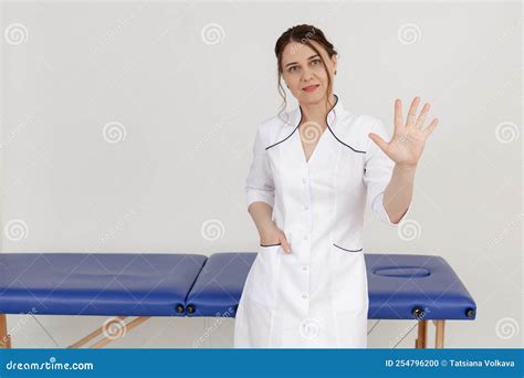 Portrait Of Middle Aged Confident Masseuse Woman Standing Near Blue Couch Stretching Hand