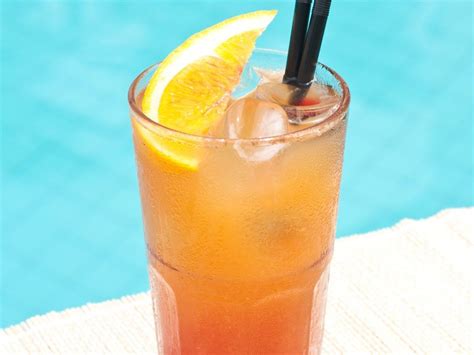 A Drink With Orange And Straws Sitting On A Towel Next To A Swimming Pool
