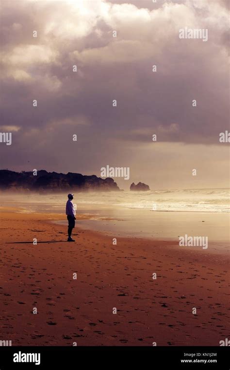 Single Man On A Beach Facing The Oceans Eternity On A Cloudy And Sandy