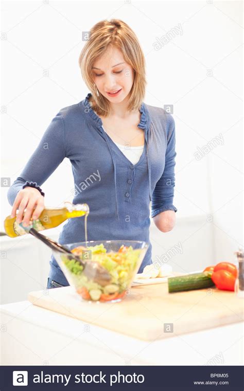 Young Woman With Amputee Arm Making Salad In Kitchen Stock Photo