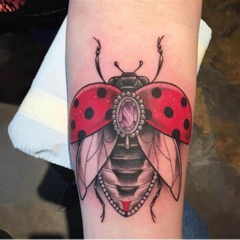 a ladybug tattoo on the arm with a red and black beetle sitting on it
