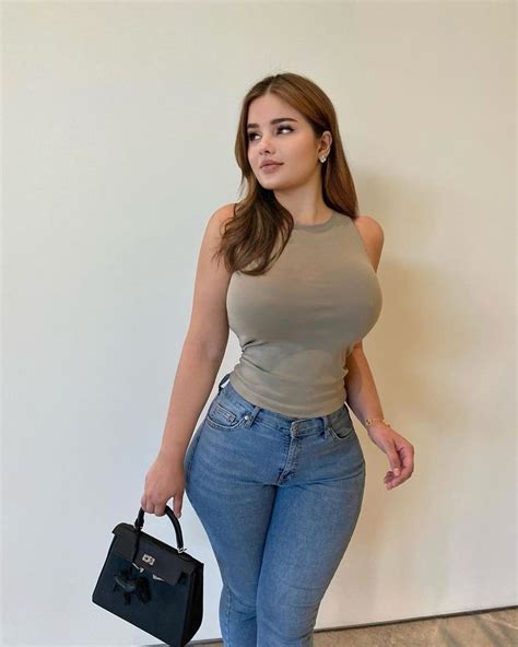 A Woman In High Rise Jeans Holding A Black Bag And Posing For The