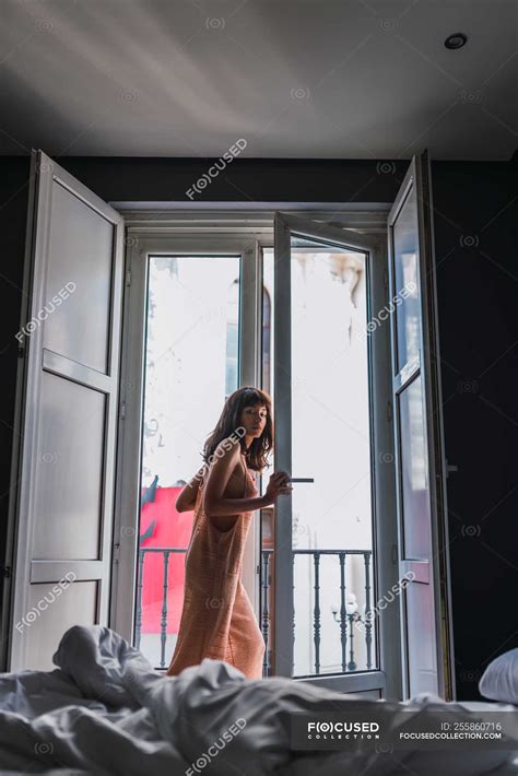 Jeune femme mince en robe nue debout près du balcon dans la chambre