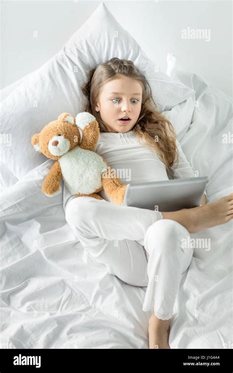 Cute Little Girl In Pajamas Using Digital Tablet While Lying In Bed