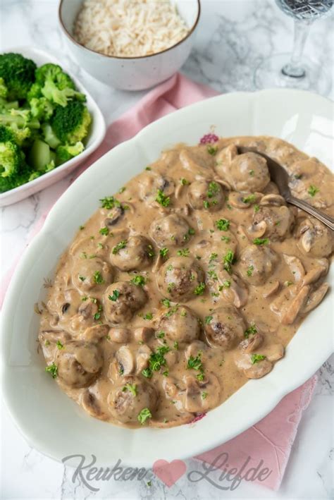 A White Plate Topped With Meat And Mushrooms Covered In Gravy Next To