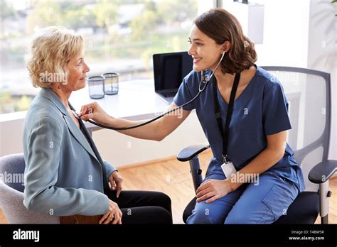 Female Doctor Wearing Scrubs In Office Listening To Senior Female