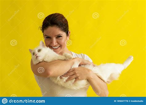happy middle aged caucasian woman with a white cat on a yellow background the female owner