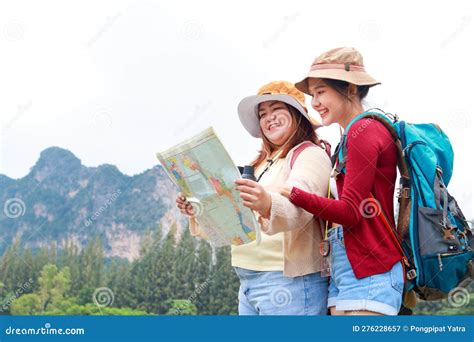 portrait of two asian female travelers carrying backpacks standing looking at map to travel