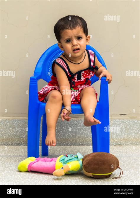 Portrait Of Indian Cute Baby Girl Sitting On Blue Chair And Playing