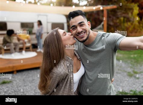 Loving Multiracial Couple Taking Selfie Near Motorhome Hugging And Kissing Resting With Their