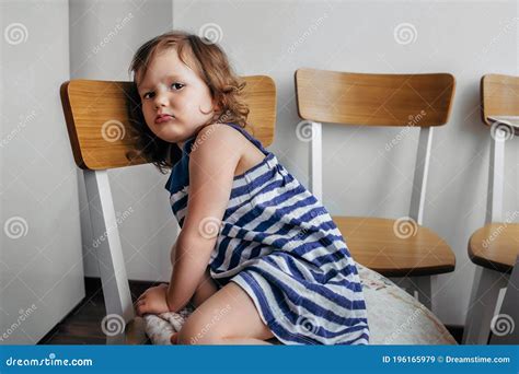 Child Girl Sitting On A Chair And Looking Sadly At The Camera Stock