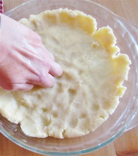 A Person S Hand On Top Of A Pie Crust In A Glass Bowl