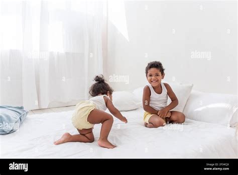 Frère et soeur Afro Américains jouent ensemble sur un lit blanc dans un loft intérieur Les