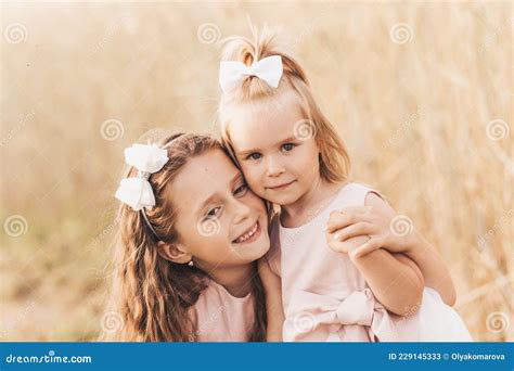 Two Cute Little Girls In Dresses Hugging In Nature In The Summer Stock