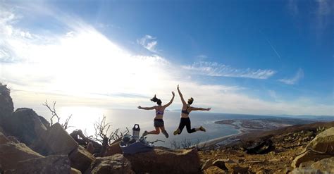 Two People Jumping In The Air On Top Of A Rocky Hill With Water And