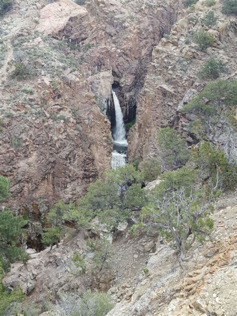 There Is A Waterfall Coming Out Of The Side Of A Mountain With Trees