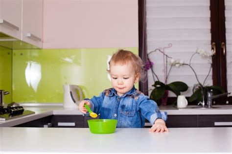 Premium Photo Cute Baby Child Eats Food Himself With Spoon In The Kitchen