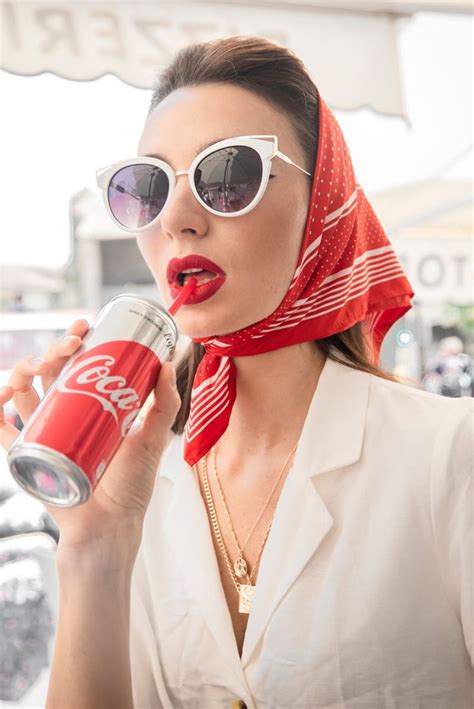 a woman wearing sunglasses and a scarf holding a coca cola can in her hand