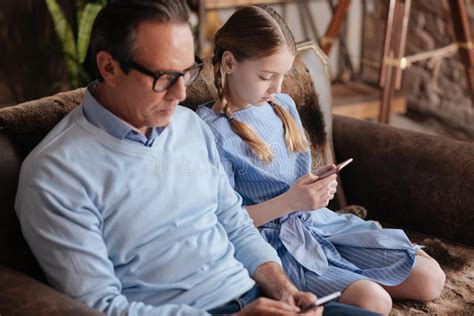 Senior Grandfather And Granddaughter Starring At Smartphones Indoors