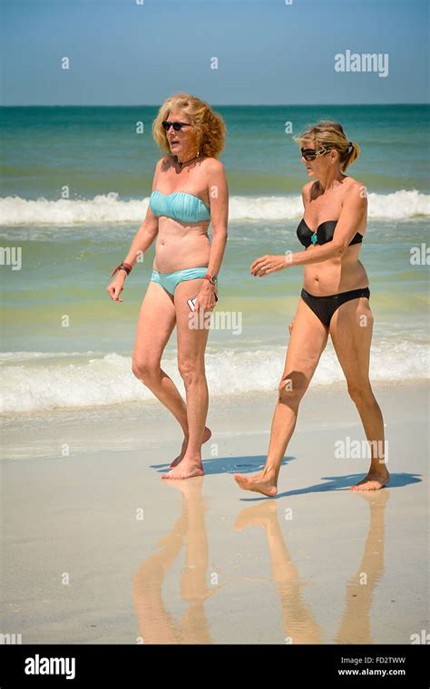 Two Older Middle Aged Women In Bikinis Stroll The Beach Conversing