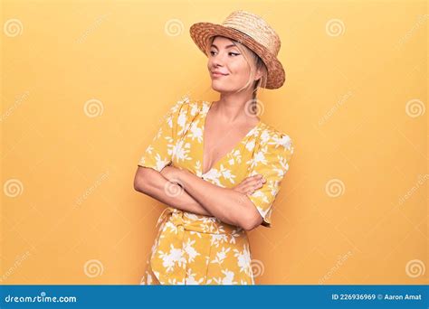 Beautiful Blonde Woman On Vacation Wearing Summer Hat And Dress Over Yellow Background Looking