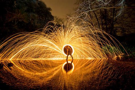 Long Exposure Of Silhouette Of Human With Burning Round And Fireworks