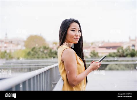 Beautiful Woman Holding Smart Phone While Standing On Elevated Walkway