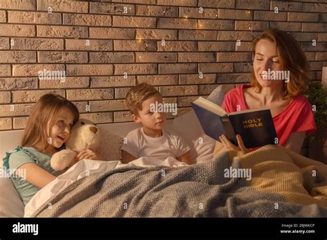Madre Leyendo La Biblia A Sus Hijos Pequeños En La Cama Fotografía De