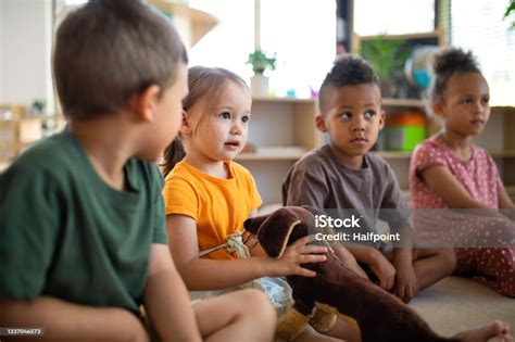 Group Of Small Nursery School Children Sitting On Floor Indoors In