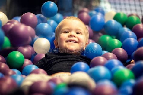 Blonde Little Boy Lying On Multi Coloured Plastic Balls In Big Dry