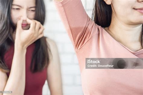 asian woman having problem sweat under armpit with friend smelling stink in background stock