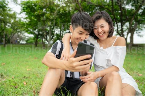 happy laughing asian lesbian couple sitting outdoor in the park while using mobile phone photo
