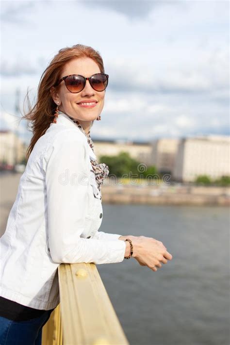 Young Fashionable Redhead Woman In Sunglasses Smiling On Bridge Stock