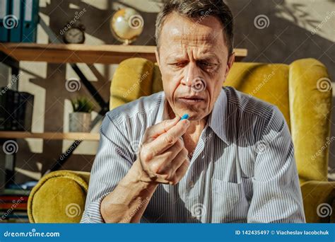Old Unpleasant Man Looking At The Blue Capsule In His Hand Stock Image