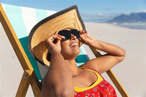 Smiling Mixed Race Woman On Beach Holiday Sitting In Deckchair Wearing